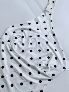 Detailed flat lay of white one-shoulder top with classic black polka dot pattern