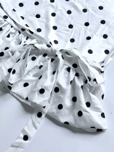 Detailed view of white polka dot dress featuring a bow waist tie and ruffled hemline