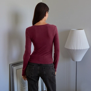Detail view of the back of a slim fit burgundy long sleeve t-shirt in a home setting