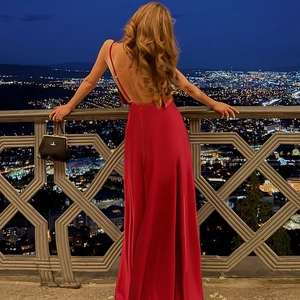 Rear view of a red backless satin evening gown with thin straps against city night lights