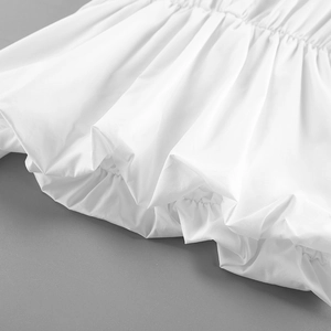 Close-up of elastic ruffled hem and shirred waist detail on white cotton blouse