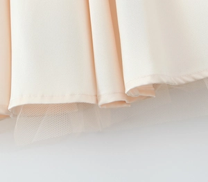 Detailed view of pale pink A-line dress hem with layered tulle mesh and neat stitching