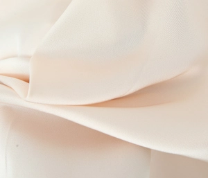 Close-up of cream satin fabric with soft sheen and delicate pleated texture on a mini dress