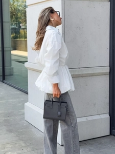Women's white long sleeve shirt with cinched waist and flared hem paired with jeans