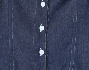 Close-up of dark blue denim dress featuring white buttons and contrast stitching detail