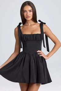 Detail of elegant black satin mini dress with bow-tie shoulder straps and pleated square neck