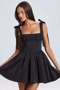 Detail of black mini dress featuring bow-tie straps and pleated waist with flared skirt