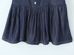 Detailed view of high-waist pleated denim dress hem with white button and fine stitching