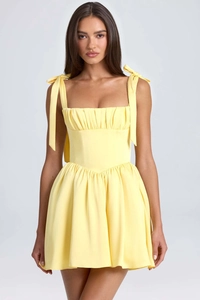 Detailed view of yellow mini dress featuring adjustable bow straps and pleated bust design