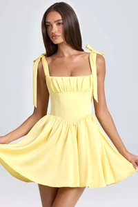 Detail of the pale yellow square-neck mini dress showing ruched chest and bow-tie straps