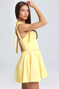 Close-up of a lemon yellow A-line dress featuring bow tie straps and pleated bodice detail
