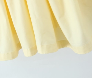 Dettaglio dell'abito giallo chiaro con cuciture dell'orlo precise e texture del tessuto
