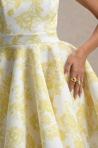 Détails de la robe à fleurs jaunes avec taille haute plissée et bijoux dorés élégants