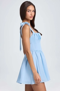 Detail of light blue mini dress featuring bow-tie straps and pleated bust structure