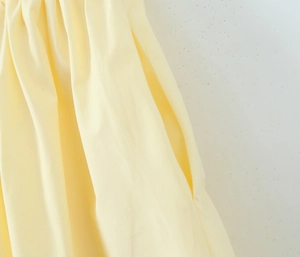 Dettaglio della tasca laterale e delle pieghe in vita sull'abito primaverile giallo chiaro