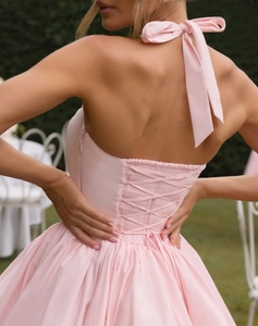 Detailed back view of a pink halter dress featuring criss-cross straps and bow tie design