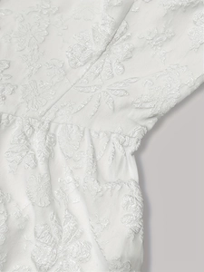 Détail du tissu jacquard blanc avec textures florales en relief et coutures fines