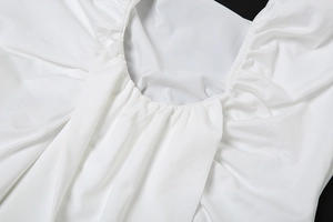 Close-up of elegant pleated V-neckline on white backless dress with woven fabric texture