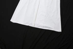 Detail view of white dress hem with front slit design on black textured fabric