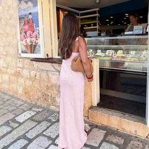Détail du dos d'une robe en mousseline rose pâle avec pochette en paille et bracelet