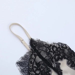 Detail of adjustable straps and black eyelash lace trim on a beige satin cropped camisole