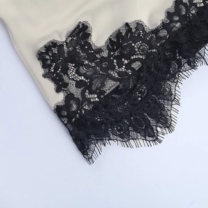 Close-up of beige satin fabric featuring delicate black eyelash lace trim detail