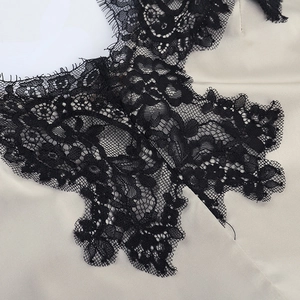 Detailed close-up of champagne satin fabric with intricate black eyelash lace trim
