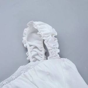Detail of white cotton shirt featuring elegant ruffle shoulder straps and lace cutouts