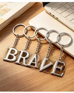 Silver metal keychains spelling BRAVE on a wooden desk with a minimalist background
