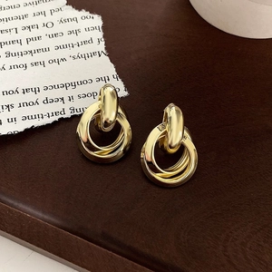 Detail of gold triple-loop metal earrings with polished finish on leather surface