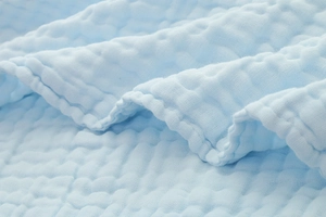 Detailed macro view of soft light blue crinkled cotton fabric with premium edge stitching