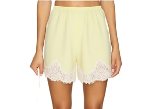 Detail of light yellow shorts featuring white lace trim hem and pleated elastic waistband
