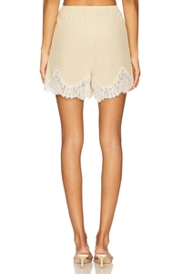 Detail of high-waist beige satin shorts with delicate white lace trim on the hem