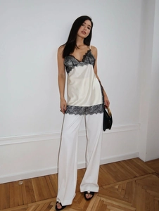 Detail of silk camisole with black lace trim and white wide-leg trousers on model