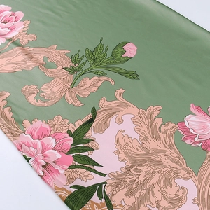 Close-up of floral fabric with pink peonies and baroque swirls on green satin texture