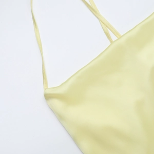 Detail of light yellow satin dress featuring delicate thin straps and a draped neckline