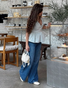 Detail of white polka dot V-neck top with ruffle hem paired with high waist wide-leg jeans
