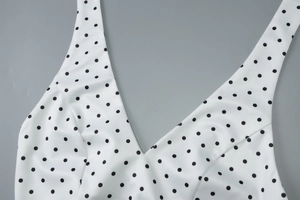 Detail shot of deep V-neck cut and classic black polka dot pattern on white fabric