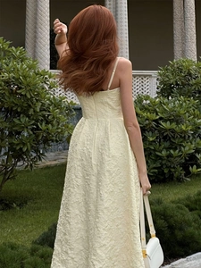 Outdoor back view of a light yellow textured midi dress with delicate spaghetti straps