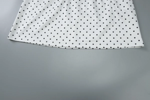 Close-up of the hemline on a white polka dot dress with precise double-needle stitching