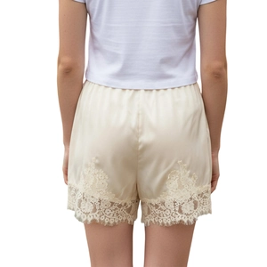 Detail of delicate lace trim on beige silk-like wide-leg shorts with an elastic waist