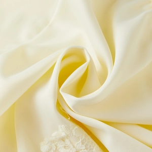 Detail view of cream satin fabric with exquisite lace trim and soft pearlescent luster