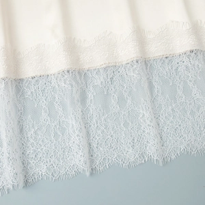 Dettaglio ravvicinato dell'orlo in pizzo bianco su un'elegante gonna midi in raso crema