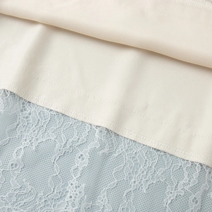 Dettaglio del tessuto color crema cucito con delicato pizzo floreale azzurro chiaro