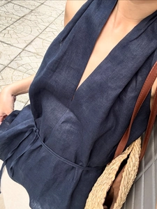 Detail of navy blue linen wrap top with V-neckline and straw woven shoulder bag texture