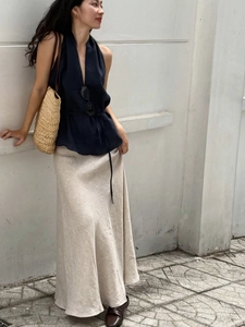 Detail of elegant navy V-neck halter top paired with beige linen maxi skirt and straw bag