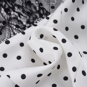 Detailed close-up of white satin fabric with black polka dots and delicate lace trim