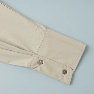 Detailed close-up of beige cotton shirt cuff with double-button and pleated texture