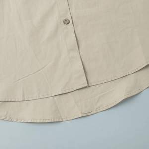 Detail of the cotton shirt hem with vintage button and fine stitching in beige
