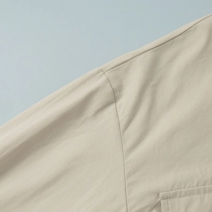 Detail view of cotton shirt shoulder seams and pocket stitching on light beige fabric
